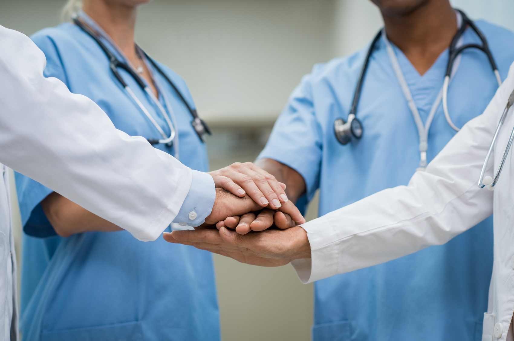 Mature doctors and young nurses stacking hands together at hospital. Close up hands of medical team stacking hands. Group of successful medical doctors and nurses stack of hands.